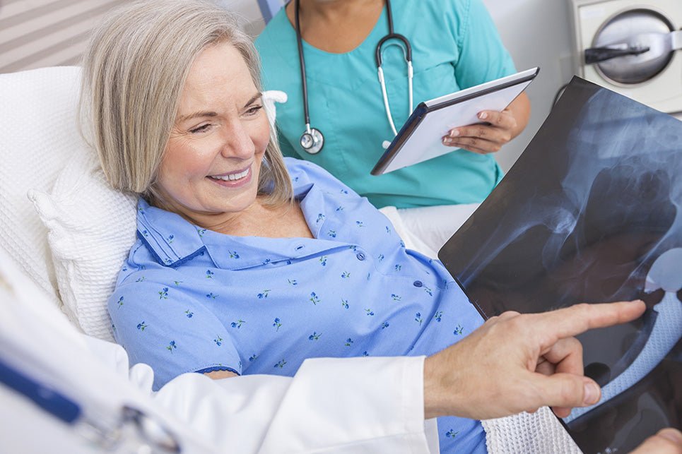 Happy senior woman in a hospital bed with a doctor looking at a hip replacement x-ray