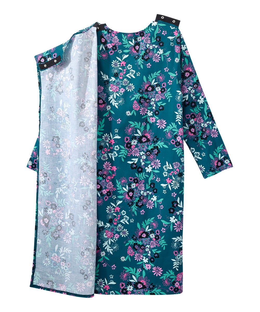 A long-sleeve tunic dress with a split design: one side features a dark teal floral print with pink, purple, and green flowers, while the other side shows a light gray floral lining. It has black shoulder straps with silver buttons at the neckline.