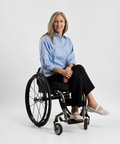 Woman in a wheelchair wearing a blue shirt and black pants on a white background
