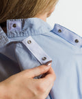 Close-up of a person wearing a light blue denim shirt with a hand adjusting the collar.